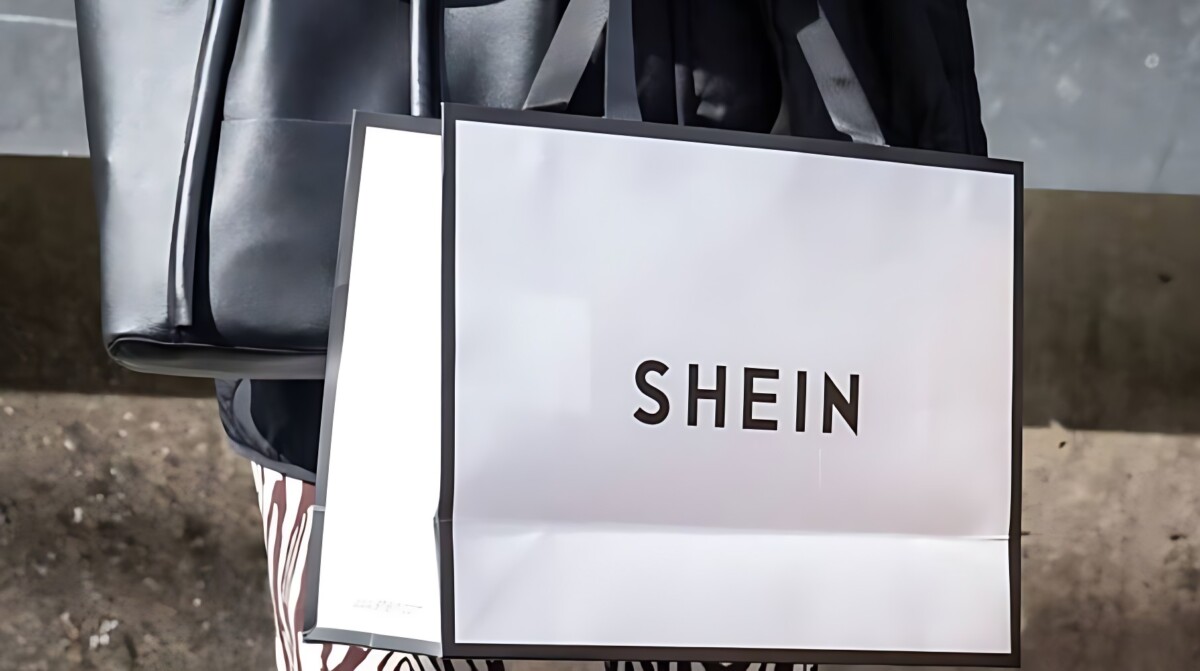 Primer plano de una bolsa de compras blanca con el logotipo de Shein en letras negras, simbolizando la presencia del minorista de moda rápida en el mercado brasileño.